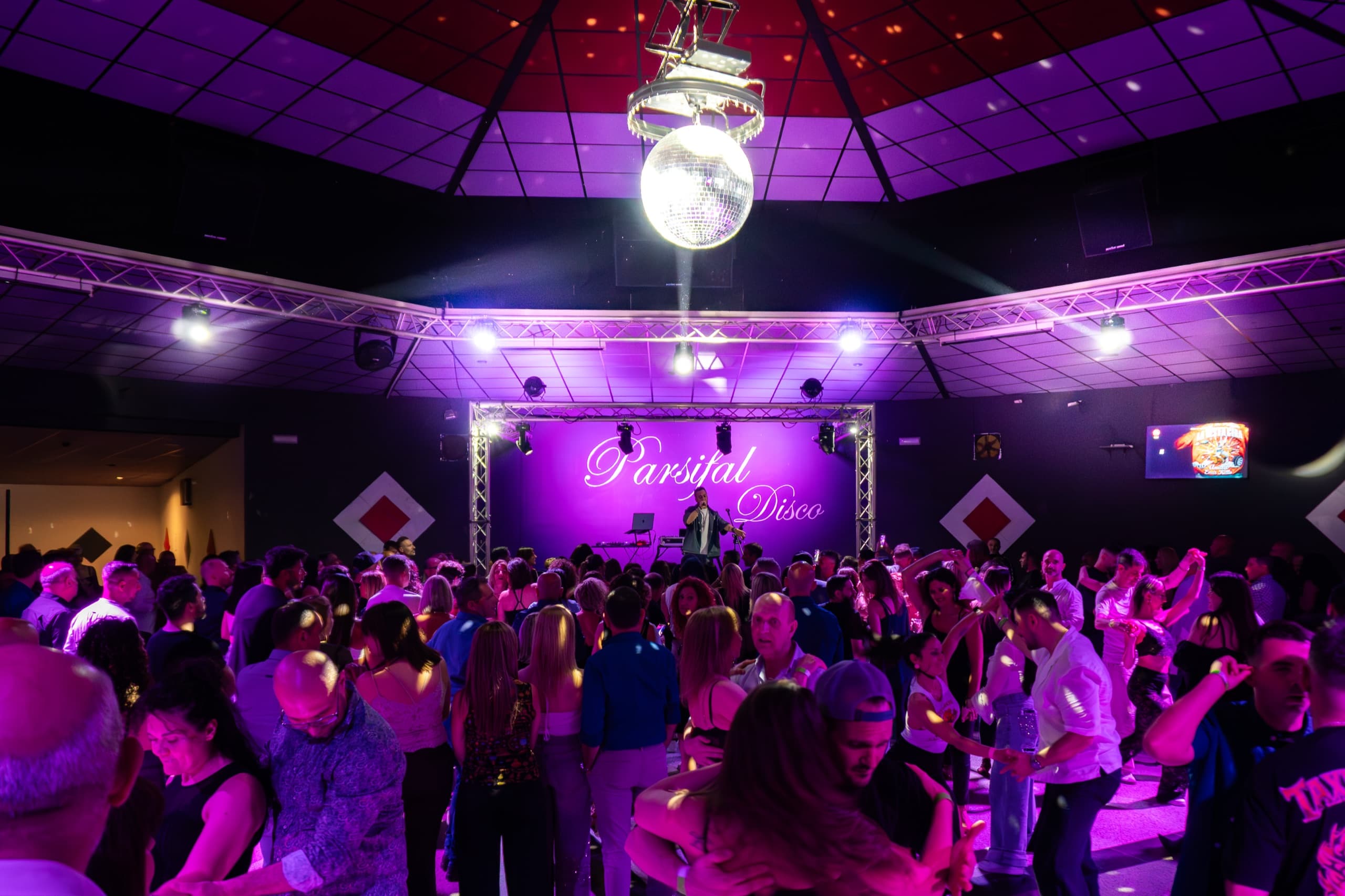 Sala del Parsifal affollata sotto una sfera specchiata e luci viola